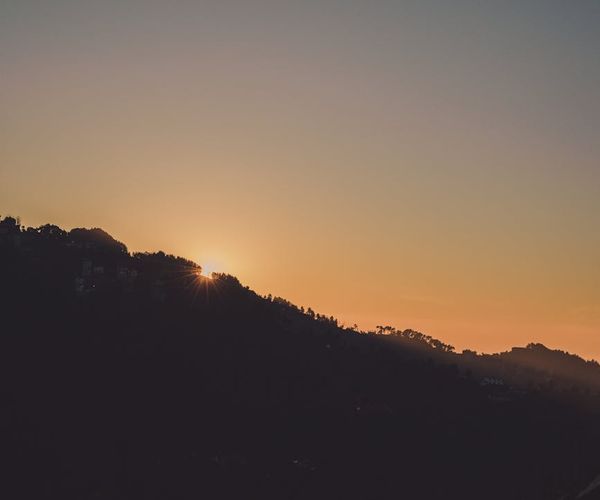 Silhouette of a person stretching during a vibrant sunrise over a mountain landscape.