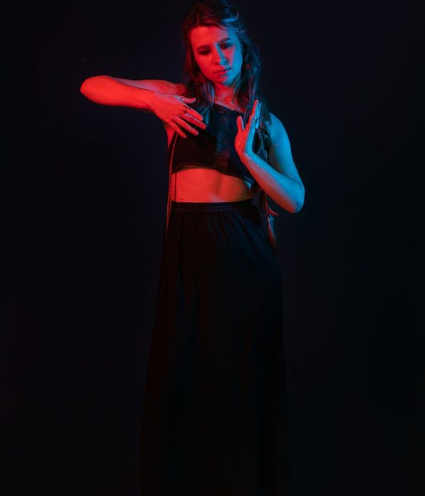 Woman performing a graceful yoga pose in a dark, minimalist studio with azure light.
